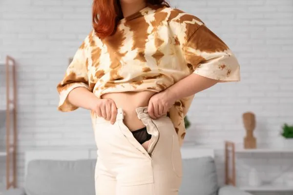 Image of woman trying to do her trousers up after pregnancy weight gain Thame